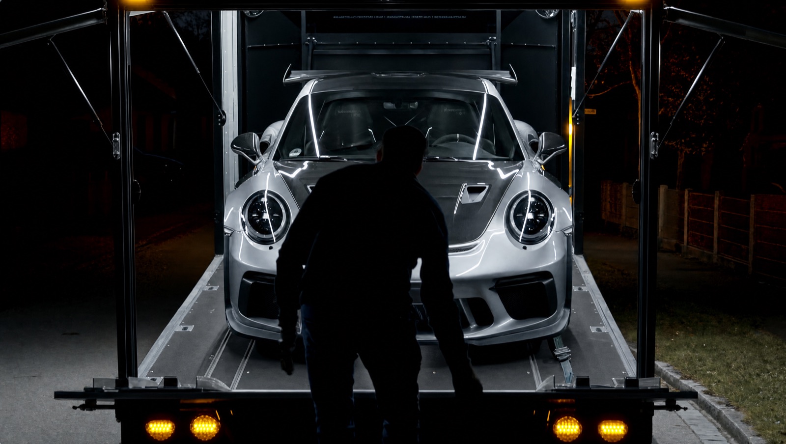 Silberner Porsche 911 GT3 RS wird nachts in einen geschlossenen Transportanhänger verladen