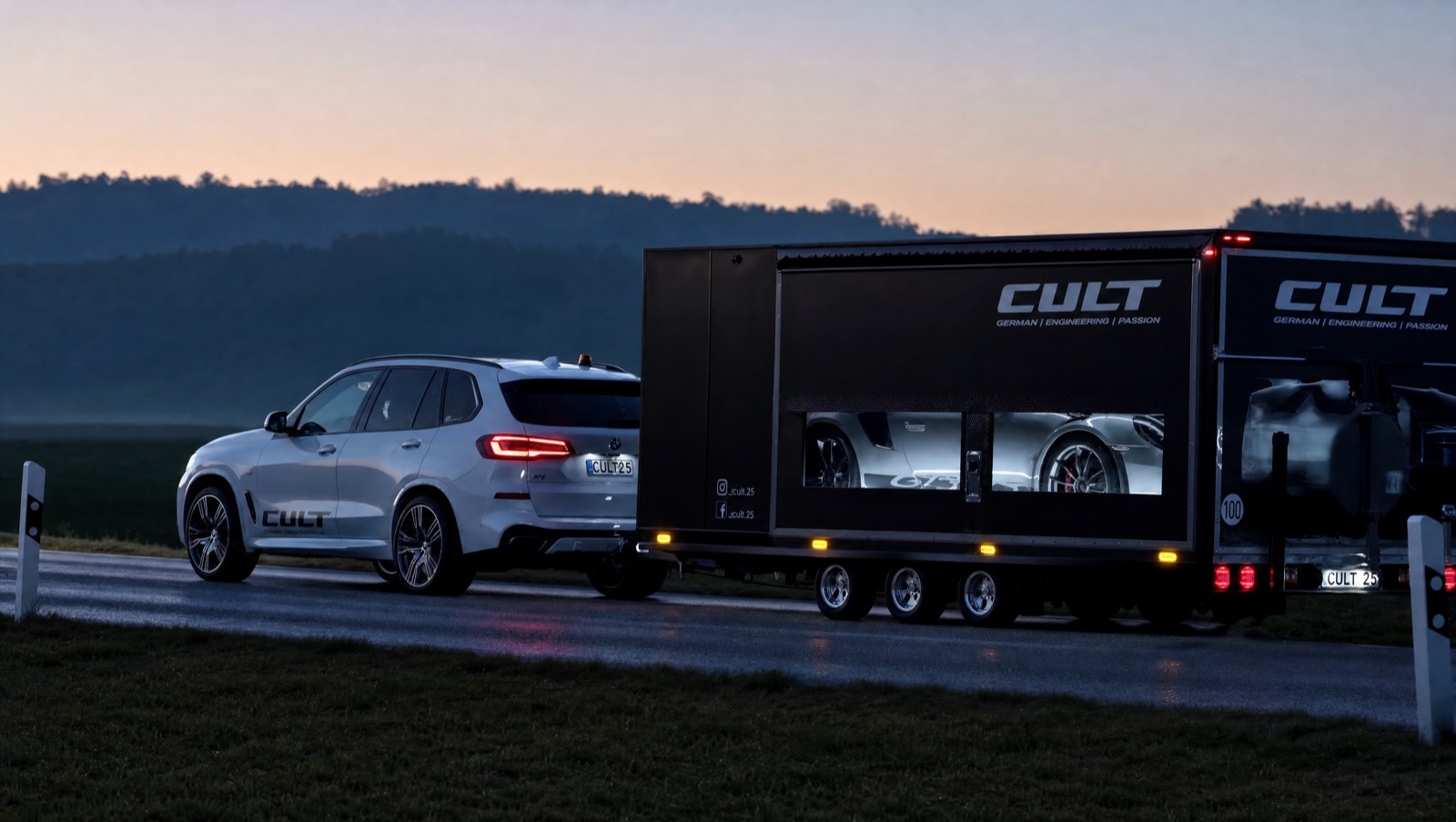 CULT-Begleitfahrzeug zieht in der Abenddämmerung einen geschlossenen Anhänger mit einem Supersportwagen im Inneren